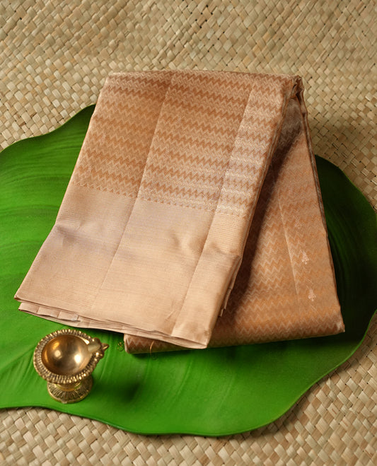 Muted Brown colour Vasundhara silk saree adorned with all-over self coloured zigzag motifs on the body, complemented by a self coloured with gold line motifs border and paired with a matching blouse piece.