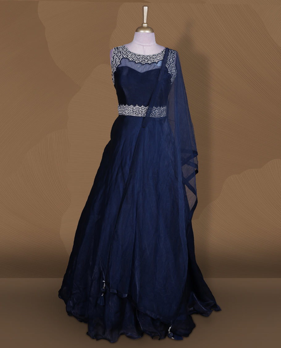 Navy blue colour Gown with stitched sleeveless embellished blouse featuring sheer yoke and waist detailing, matching stitched flared lehenga with tassel accents, and plain sheer dupatta.