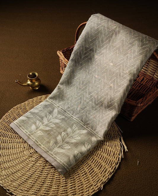 Olive sage colour semi tussar saree adorned with Cream Zigzag printed pattern across the body and Leaf pattern on contrast olive sage colour border, paired with a matching blouse.