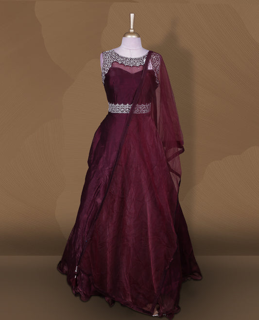 Wine colour Gown with stitched sleeveless embellished blouse featuring sheer yoke and waist detailing, matching stitched flared lehenga, and plain sheer dupatta.