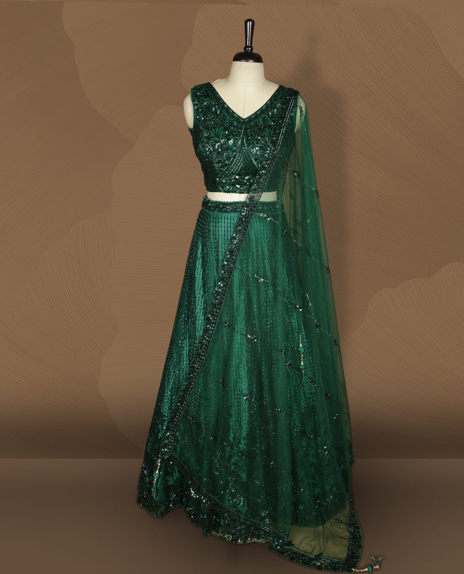 Emerald green colour lehenga set with stitched sleeveless V‑neck heavily sequinned blouse featuring cut‑out tie‑up back, matching stitched flared lehenga, and net dupatta with sequin border and scattered floral motifs.