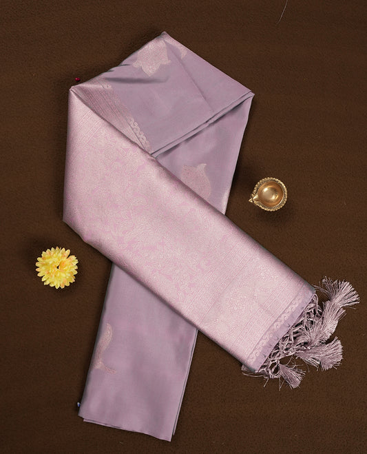 Dusty Lilac Semi Silk Saree with Subtle Zari Butta Motifs, Matching Pastel Lilac Zari Woven Pallu and Border with Intricate Floral Patterns and Tassels, Paired with Coordinated Blouse Piece