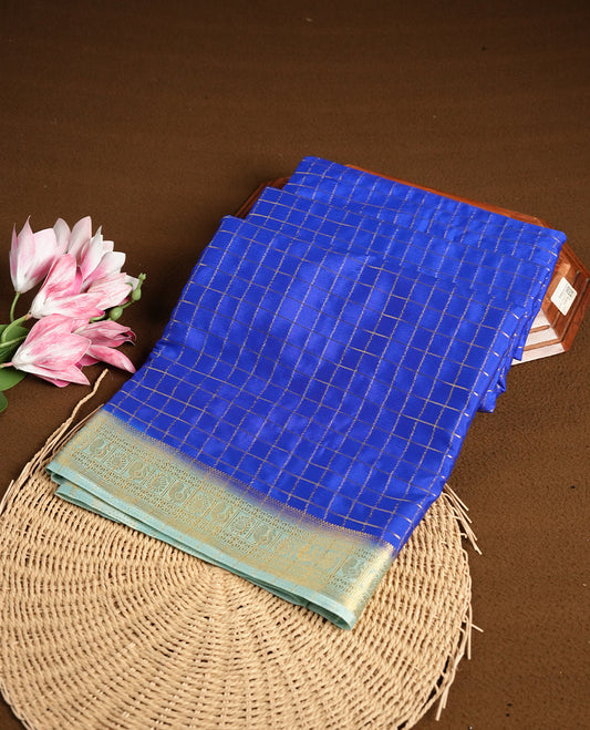 Blue colour mysore crepe saree with gold zari check pattern on body, complemented by contrast sky blue colour border featuring peacock and chakkram motifs, paired with matching blouse.