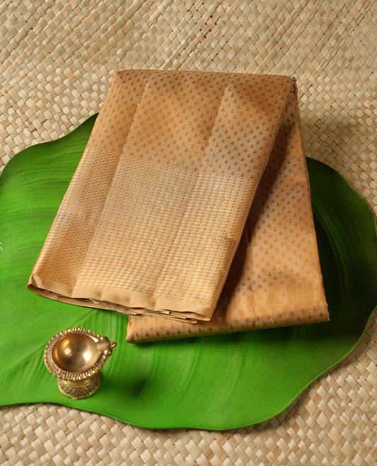 Muted Brown colour Vasundhara silk saree adorned with all-over self coloured motifs on the body, complemented by a self coloured with tiny daimond pattern with gold tree motifs border and paired with a matching blouse piece.