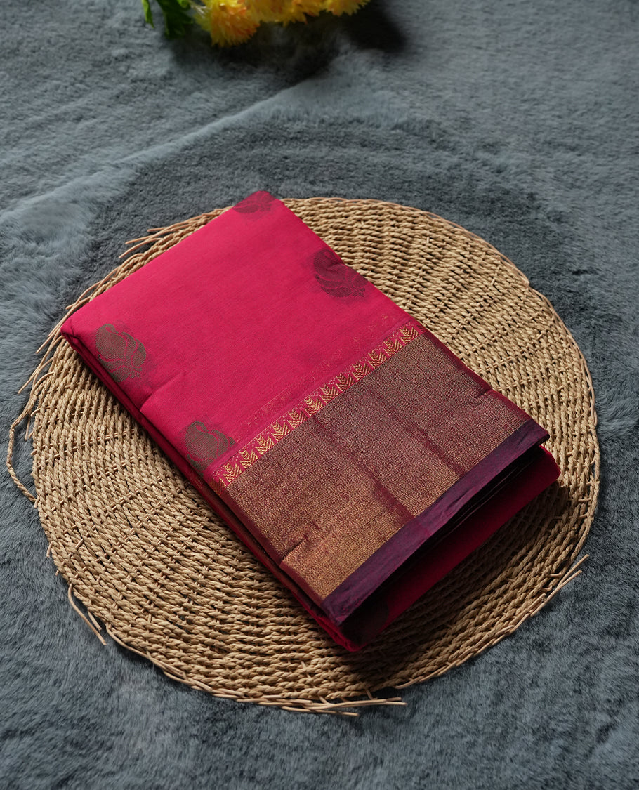 Rani Pink colour Silk Cotton Saree with Antique Copper Zari Border and Micro Geometric Edge, Body adorned with Subtle Leaf Buttas, Floral Jacquard Pallu, and a Coordinated Rani Pink Blouse with Matching Zari Border