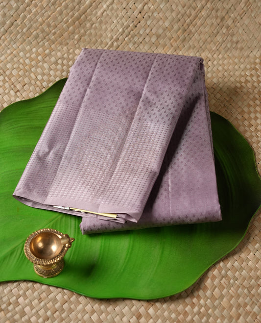 Dusty Lavender colour Vasundhara silk saree featuring self colour motifs across the body, finished with a self‑coloured tiny daimond pattern with gold tree motifs on border and a coordinating blouse.