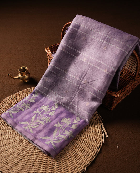 Light lavender colour semi tussar saree adorned with Cream strip printed pattern across the body, with cream Floral pattern on contrast Light purple colour border, paired with a matching blouse.
