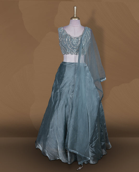 Dusty teal blue colour lehenga set with stitched sleeveless heavily embellished blouse featuring scalloped neckline, matching stitched flared lehenga, and plain sheer dupatta.