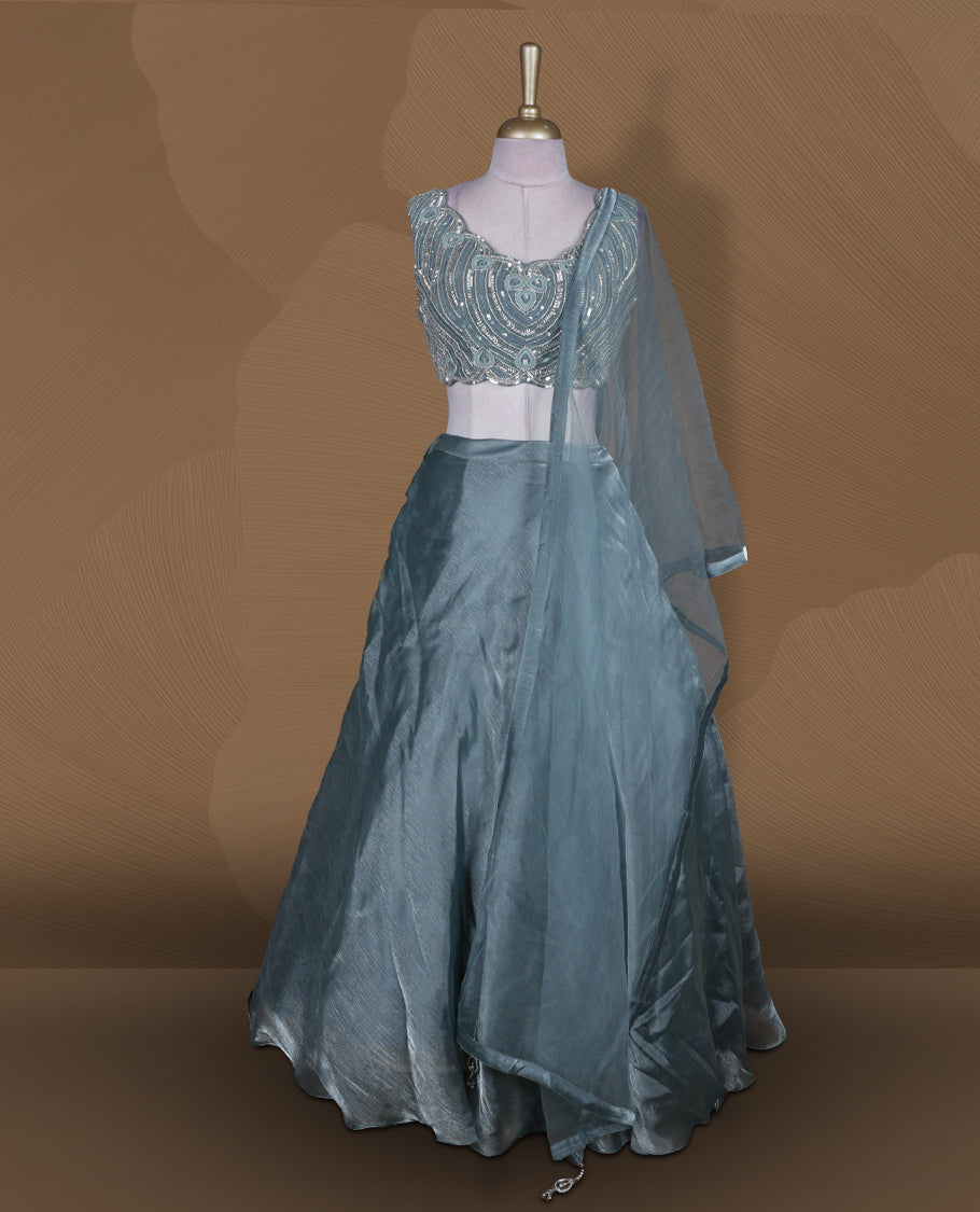 Dusty teal blue colour lehenga set with stitched sleeveless heavily embellished blouse featuring scalloped neckline, matching stitched flared lehenga, and plain sheer dupatta.