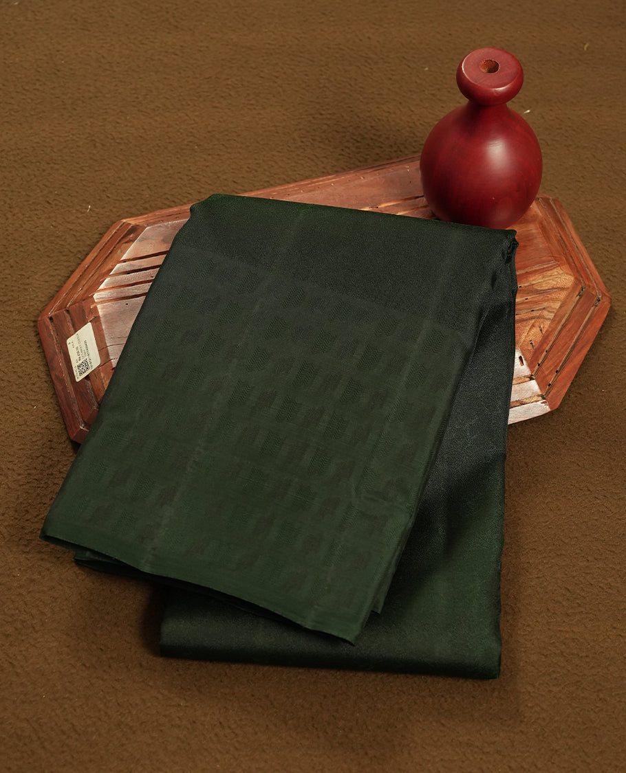 A dark green colour semi soft silk saree featuring a self coloured woven border and patterned body, complemented by self coloured pallu and a matching blouse piece.