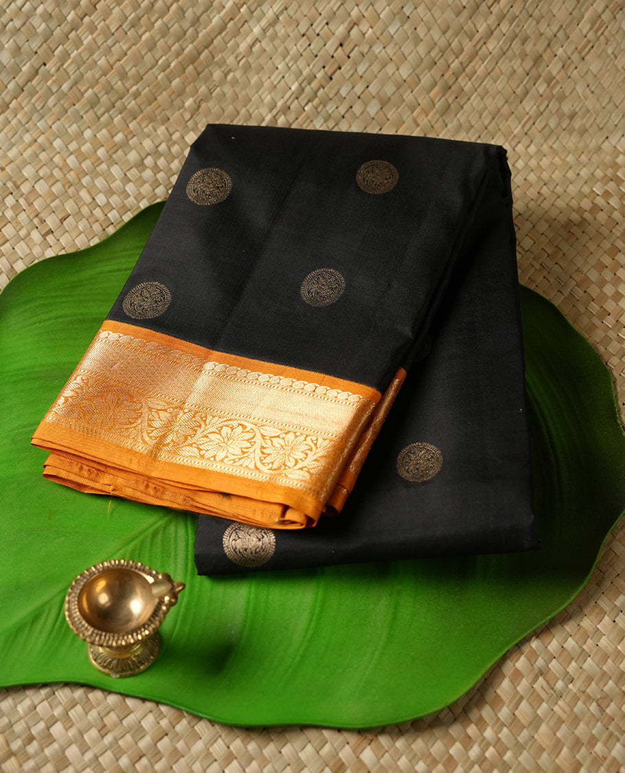 Black colour Vasundhara silk saree adorned with all-over gold chakkaram motifs on the body, complemented by a contrast turmeric colour with gold flower kodi motifs border and paired with a matching blouse piece.