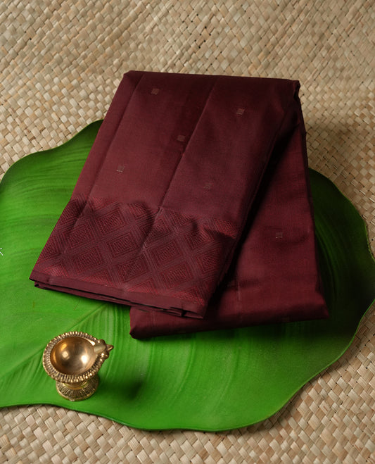 Dark maroon colour Vasundhara silk saree adorned with all-over tiny gold square motifs on the body, complemented by a self colour zari border and paired with a matching blouse piece.