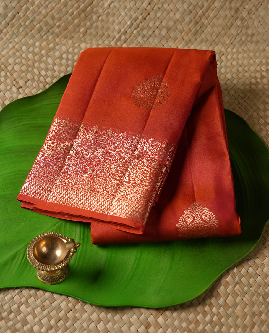 Burnt orange colour Vasundhara silk saree adorned with all-over gold motifs on the body, complemented by a self colour with gold tarditional border and paired with a matching blouse piece.