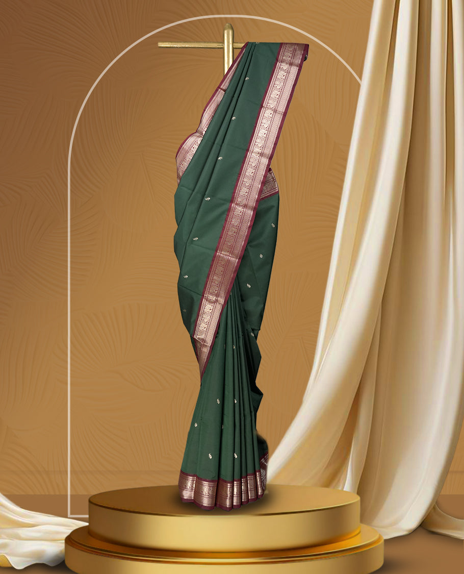 Dark green colour soft silk saree with silver buttas, enhanced by a vibrant maroon zari border and pallu, paired with a matching blouse.