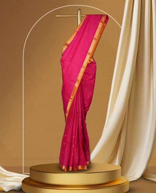 Magenta colour soft silk saree with golden buttas, enhanced by a vibrant orange zari border and pallu, paired with a matching blouse.