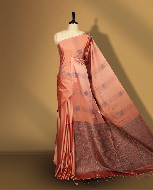 Amber rose colour semi soft silk saree, adorned with subtle self woven motifs on the body & The design is elevated with an elegant zari border & pallu with intricate detailing and tassel accents, paired with a matching blouse.