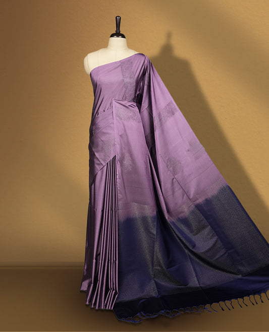Royal purple colour semi soft silk saree adorned with delicate woven floral motifs on the body, complemented by a rich contrast deep blue colour woven pallu with intricate detailing and tassel accents & Comes with a matching blouse piece.
