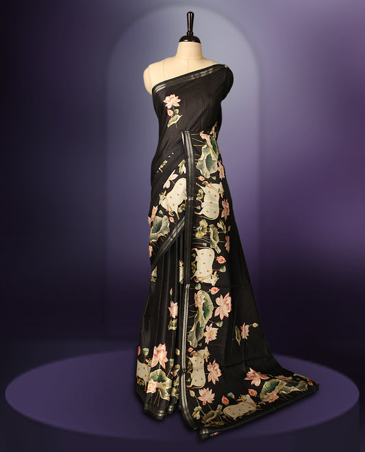 Black colour saree adorned with elegant lotus floral prints across the body and pallu, complemented by a sleek matching border, and paired with a coordinating blouse.