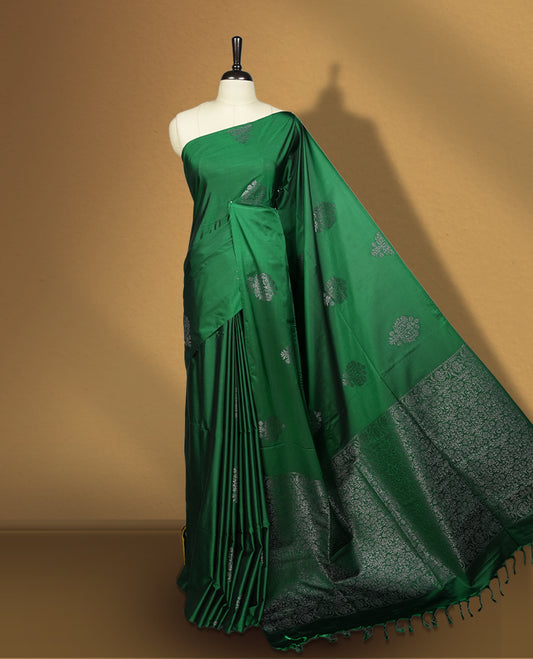 Royal Green colour semi soft silk saree adorned with delicate woven floral motifs on the body, complemented by a rich contrast woven pallu with intricate detailing and tassel accents & Comes with a matching blouse piece.