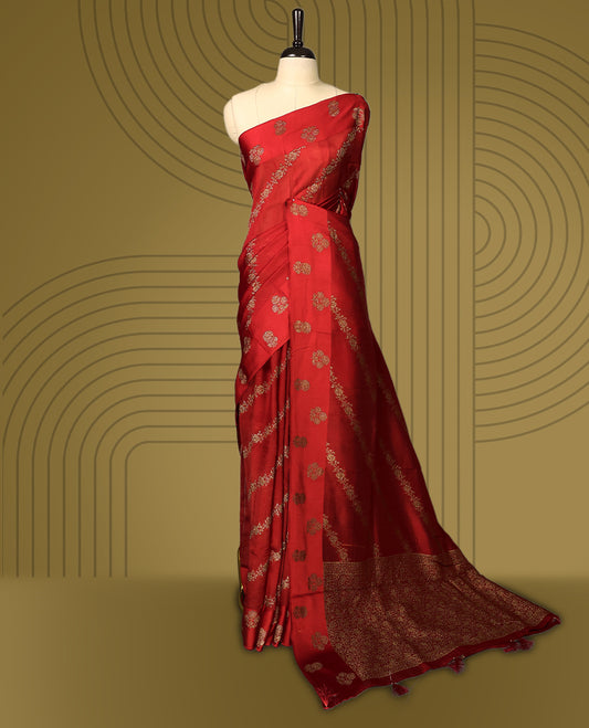 Cherry red semi Banaras tussar saree adorned with golden floral motifs in diagonal patterns across the body and a finely woven zari border, finished with a rich golden pallu, paired with a matching blouse.