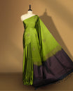 Olive green colour semi soft silk saree adorned with delicate woven self motifs on the body, complemented by a rich contrast navy blue colour woven pallu with intricate detailing and tassel accents & Comes with a matching blouse piece.