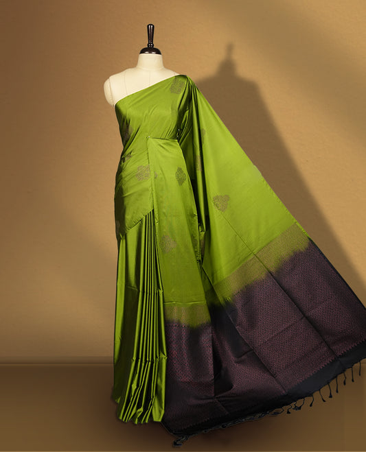 Olive green colour semi soft silk saree adorned with delicate woven self motifs on the body, complemented by a rich contrast navy blue colour woven pallu with intricate detailing and tassel accents & Comes with a matching blouse piece.