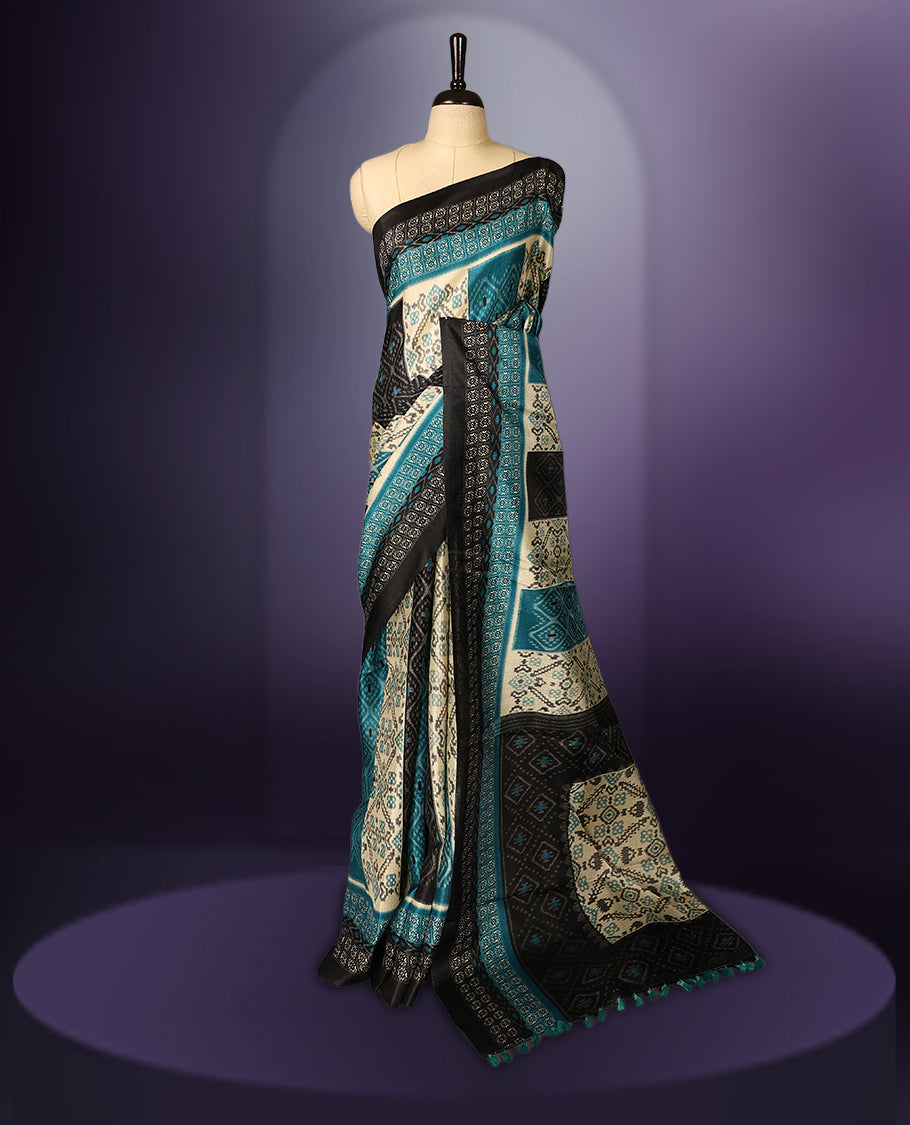 Charming teal, black, and cream printed saree featuring intricate geometric and floral designs, accentuated with a bold black border and tassel finish & paired with a matching blouse.