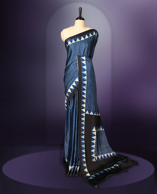 Blue colour saree featuring fine striped patterns across the body, accentuated with bold triangular designs along the border, and a contemporary pallu with geometric detailing, paired with a matching blouse.