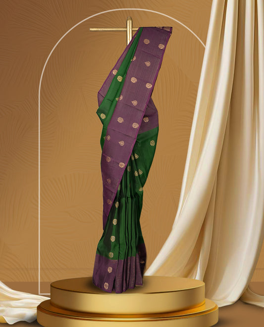 Green colour soft silk saree adorned with golden buttas, complemented by a rich purple border and pallu featuring intricate zari designs & Paired with a matching blouse.