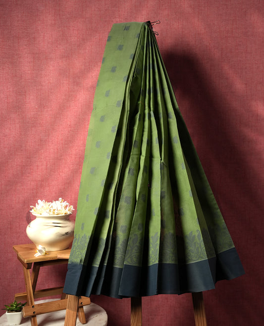 Moss green colour silk cotton saree featuring elegant floral zari motifs on the body, complemented by a rich contrast dark plain border and pallu with traditional woven detailing & Comes with a matching blouse piece.