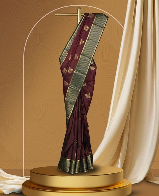 Deep maroon colour soft silk saree adorned with golden buttas, enhanced by a striking green zari border and pallu with intricate designs & Paired with a matching blouse.