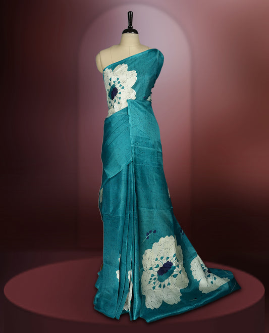 Teal blue colour saree with bold white floral motifs and subtle navy blue accents, exuding timeless elegance and modern charm, paired with a matching blouse.