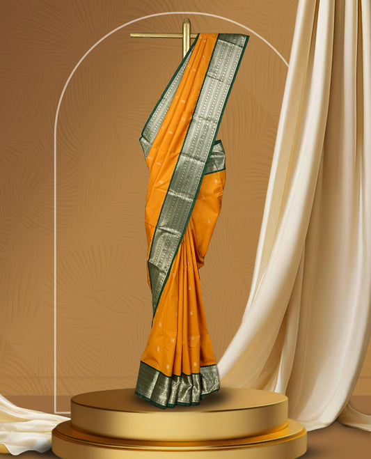 Mustard yellow colour soft silk saree adorned with golden buttas, highlighted by a rich green border and pallu with intricate zari designs & Paired with a matching blouse.