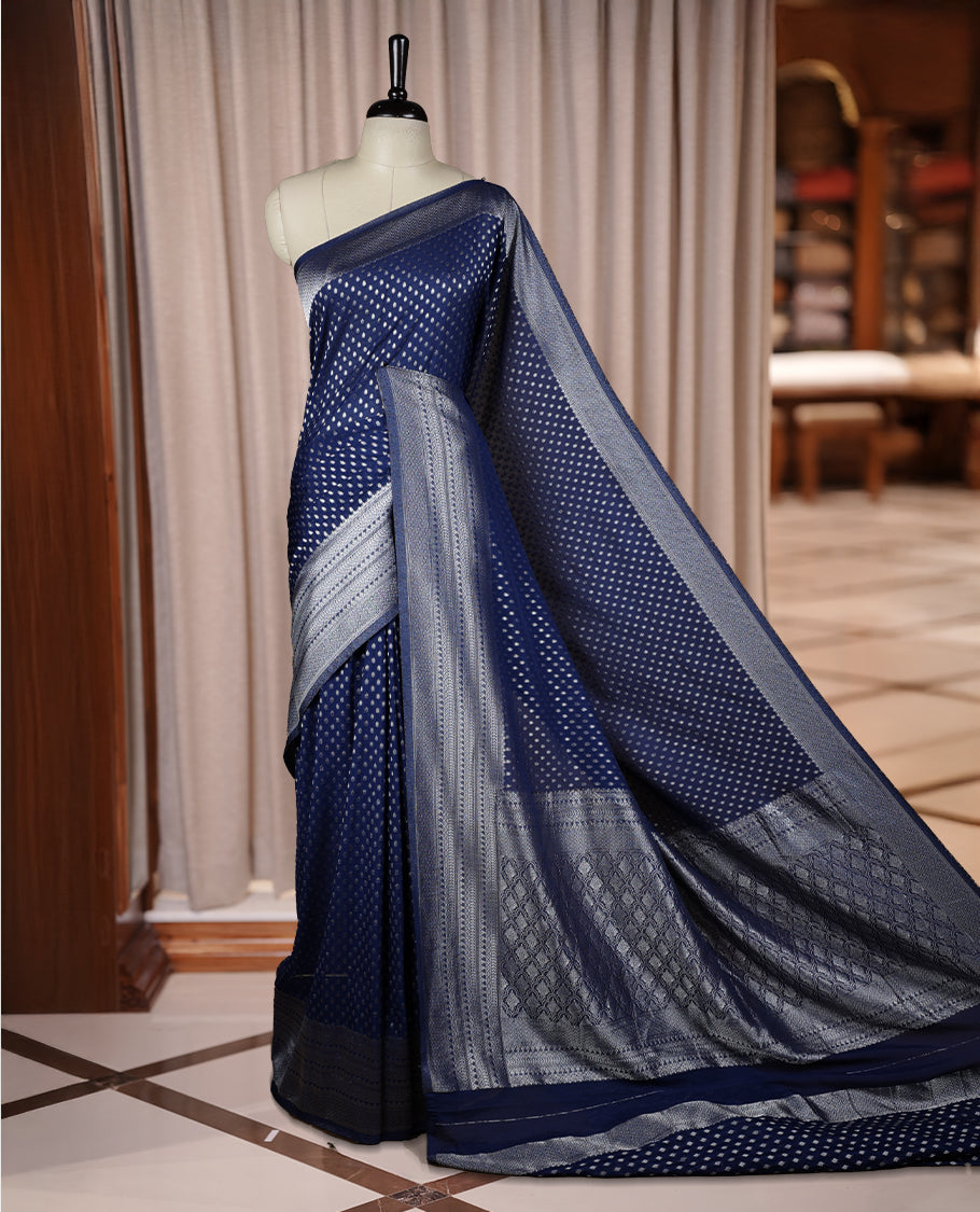 Navy blue colour Banarasi silk saree featuring intricate zari weaving and a soft silk texture, Adorned with silver motifs on the body, complemented by a rich Banarasi border and pallu & Comes with a matching blouse.