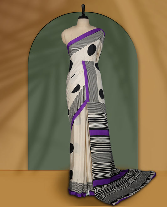 Cream colour saree with bold black polka dots and striped patterns, highlighted by a vibrant purple border & Comes with a stylish matching blouse.