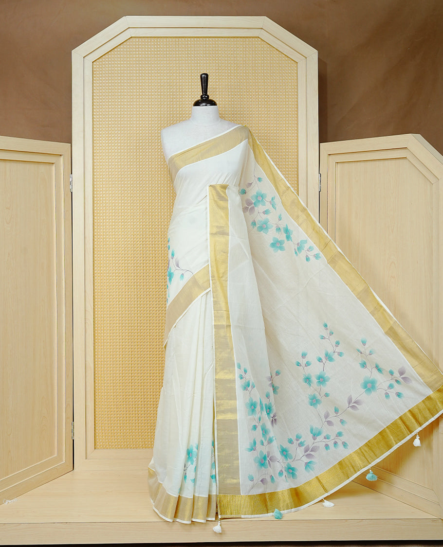 Cream Colour Cotton Kerala Saree Featuring Digital Floral Prints Across The Body, Enhanced With A Gold Zari Border, Traditional Gold Zari Pallu, Finished With Mint & White Tassels And A Matching Blouse Piece
