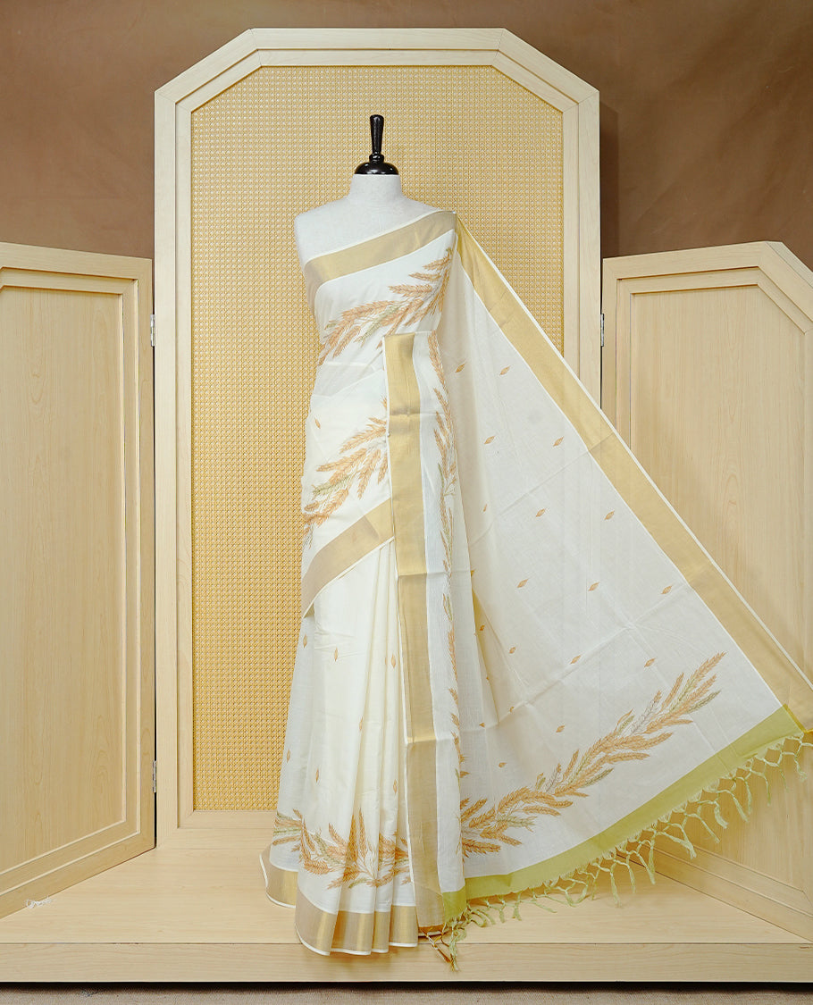 Cream Colour Cotton Kerala Saree Featuring Delicate Wheat Motifs and Scattered Leaf Designs On Body, Enhanced with a Classic Gold Zari Border. The Pallu Is Finished with Light Green Tassels and Paired with a Matching Blouse Piece.
