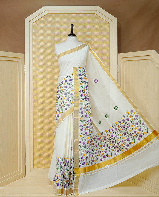 Cream Colour Cotton Kerala Saree Featuring Digital  Violet & Yellow Colour Floral Motifs On Body, With A Classic Gold Zari Border & A Gold Zari Pallu, Paired With A Matching Blouse Piece.