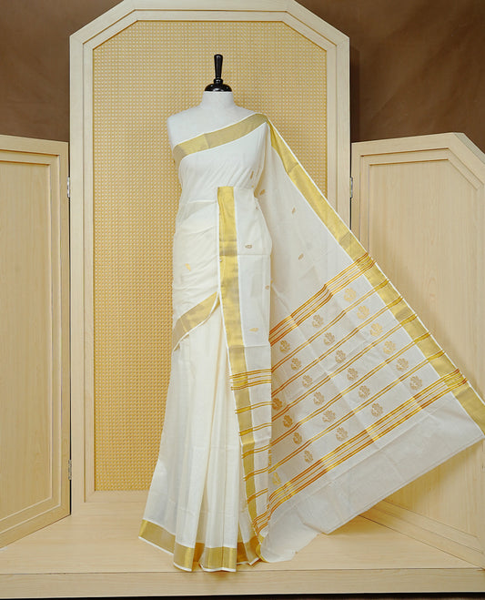 Cream Colour Cotton Kerala Saree Featuring Delicate Gold Leaf  Pattern Across The Body, Enhanced With A Traditional Gold Zari Border, A Gold Peacock Motifs &  Striped Gold Zari Pallu, Finished With A Matching Blouse Piece