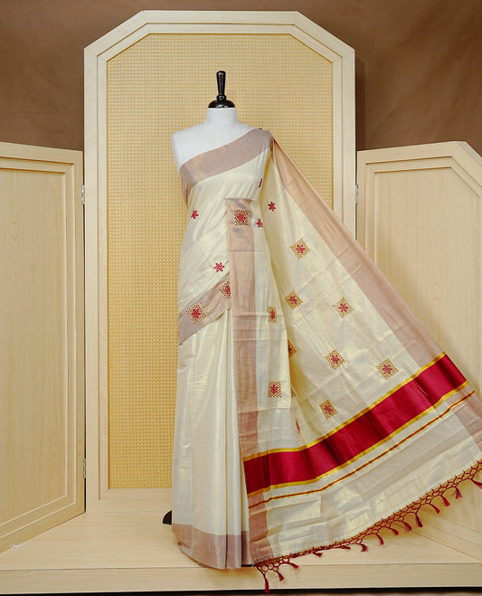 Cream Colour Tissue Kerala Saree Featuring Delicate Brick Red Floral Embroidery Work Across The Body, Enhanced With A Light Brown Zari Border And A Rich Brick Red & Gold Zari Pallu, Finished With Brick Red Tassels And A Matching Blouse Piece