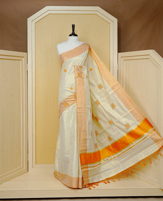 Cream Colour Tissue Kerala Saree Featuring Delicate Orange Floral Emboridery work Across The Body, Enhanced With A Light  Orange Zari Border, A Vibrant Orange And Gold Zari Pallu, Finished With Orange Tassels, And A Matching Blouse Piece