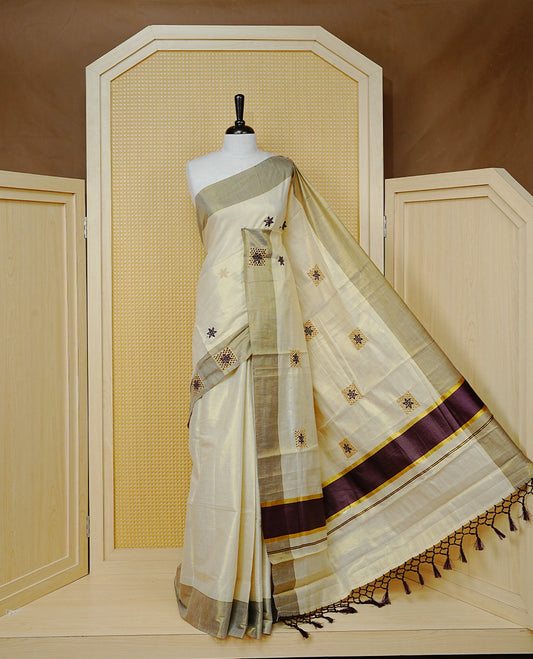 Cream Colour Tissue Kerala Saree Featuring Delicate Maroon Floral Embroidery Work Across The Body, Enhanced With A Light maroon Zari Border And A Rich Maroon & Gold Zari Pallu, Finished With Maroon Tassels And A Matching Blouse Piece
