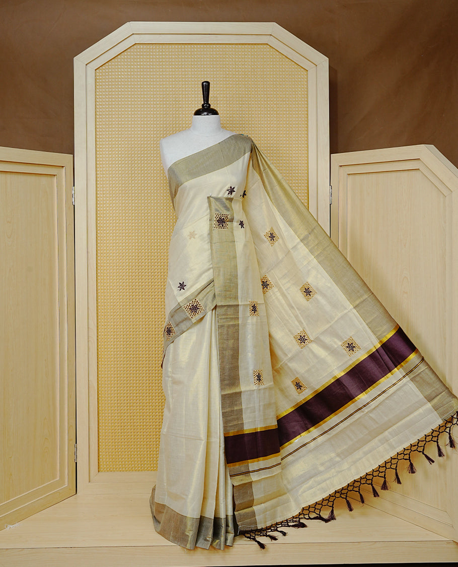 Cream Colour Tissue Kerala Saree Featuring Delicate Maroon Floral Embroidery Work Across The Body, Enhanced With A Light maroon Zari Border And A Rich Maroon & Gold Zari Pallu, Finished With Maroon Tassels And A Matching Blouse Piece