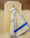 Cream Colour Tissue Kerala Saree Featuring Delicate Woven Motifs Across The Body, Enhanced With A Grey Zari Border And A Rich Blue Gold Zari Pallu, Finished With Blue Tassels And A Matching Blouse Piece