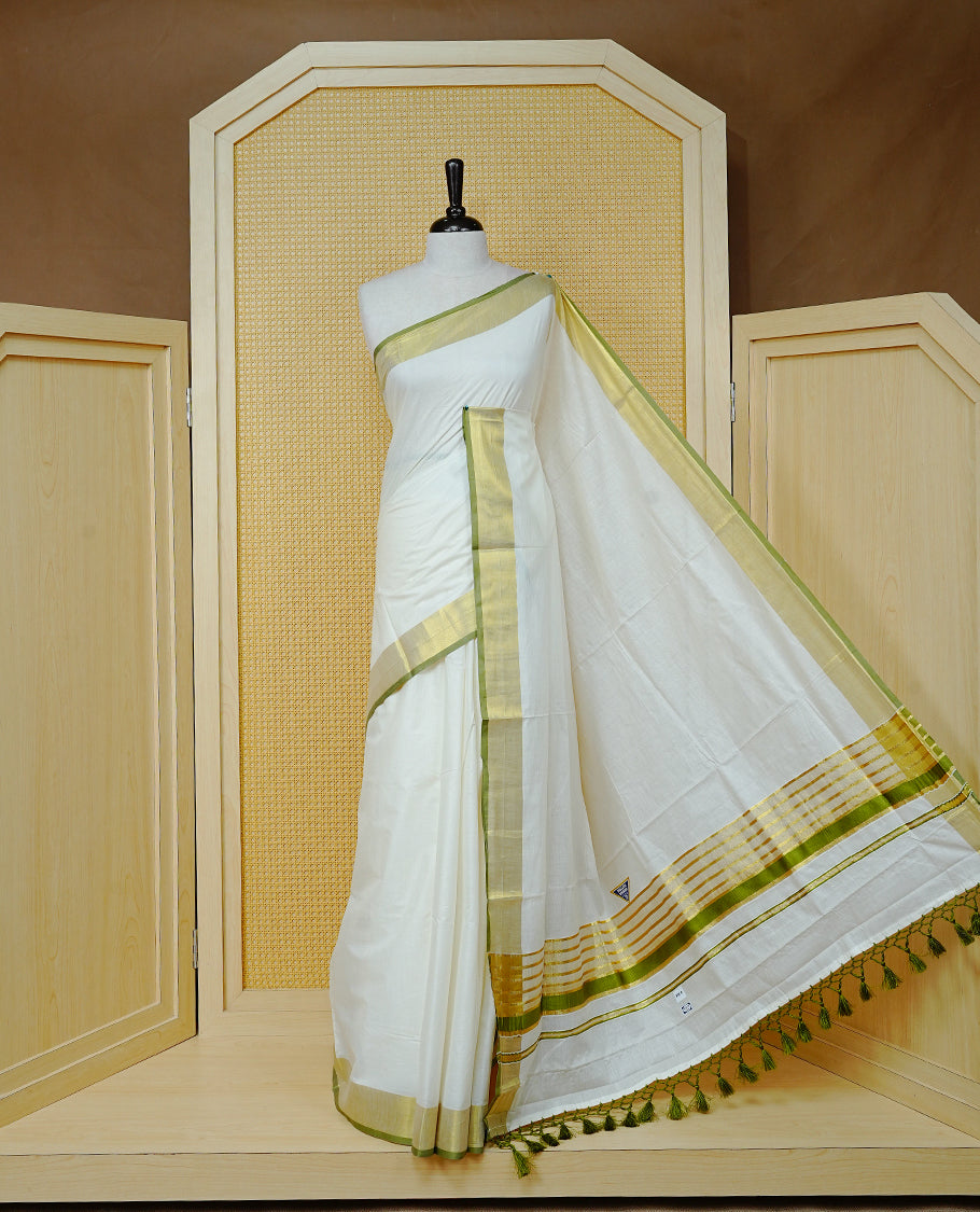 Cream Colour Cotton Kerala Saree Featuring A Plain Body, Enhanced With A Gold Zari & Light Green Colour Border, A Traditional Gold Zari Pallu, Light Green Tassels, And A Matching Blouse Piece.