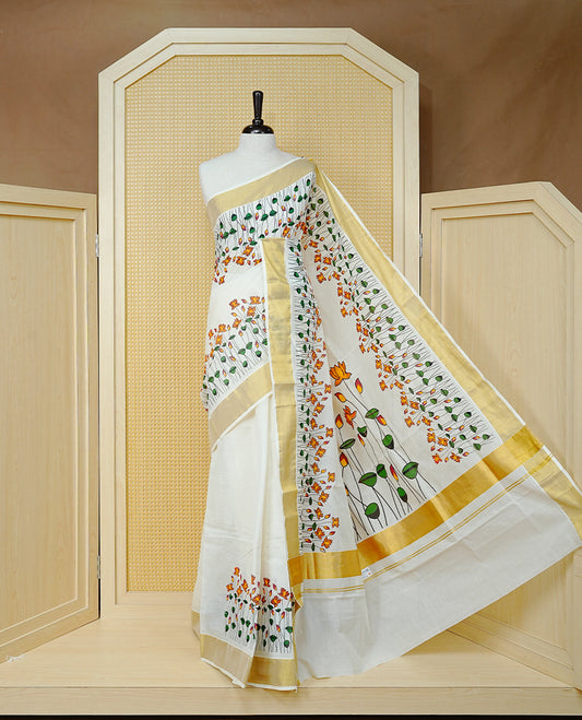 Cream Colour Cotton Kerala Saree Featuring Floral And Lotus Motifs On Body, With A Classic Gold Zari Border & A Gold Zari Pallu, Paired With A Matching Blouse Piece.