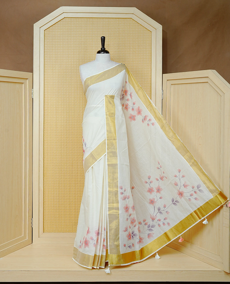 Cream Colour  Cotton Kerala Saree Featuring Digital Floral Prints Across The Body, Enhanced With A Gold Zari Border, Traditional Gold Zari Pallu, Finished With Peach & White  Tassels And A Matching Blouse Piece.