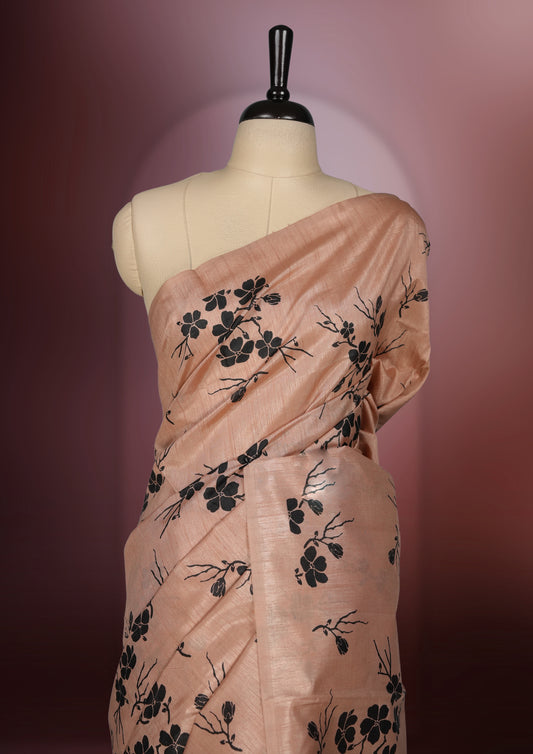 Pastel peach colour saree with delicate black floral prints spread across the body, The black pallu features coordinated floral motifs and stripes, Finished with a sleek border and paired with a matching blouse.