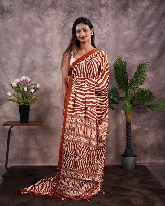 Rust Orange Colour satin model saree featuring Zibra print on body. Ajrak & zibra print on pallu with jhumka tassels, comes with contrast plain blouse piece.