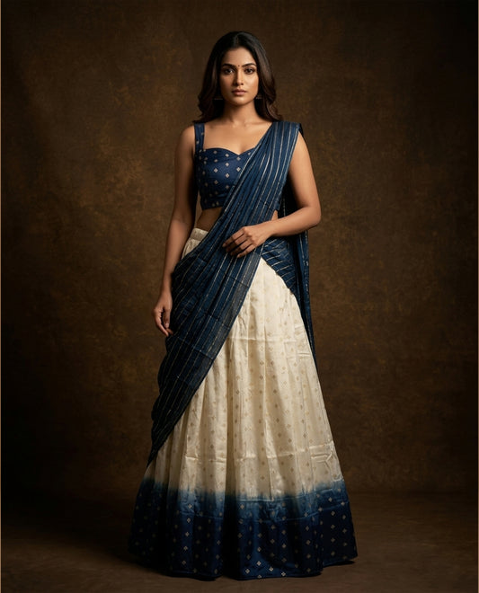 Off white colour semi stitched half saree featuring elegant zari buttas on the body, paired with a contrast blue border and matching motifs dupatta,paired with matching blouse piece.
